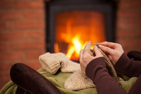 Woman knitting warm wool socks in front of fireplace - closeup on hands, shallow depthの写真素材