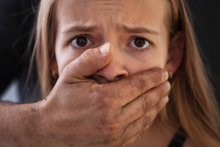 Child abuse concept - dirty male hand covering a frightened young girl mouth, closeupの写真素材