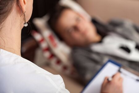 Young teenager boy at psychotherapy, lying on a sofa while counseling professional takes notes - close up, focus on foregroundの写真素材