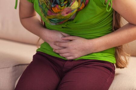 Young girl with abdominal pain holding tummy with hands - close up on torso