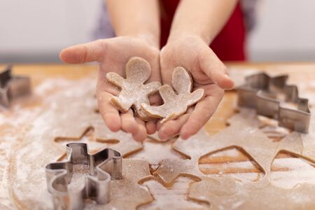 Young girl hands holding fresh cut gingerbread cookie people above the table with the dough -...