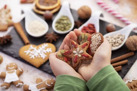 Hands holding gingerbread cookies decorated with natural seeds and dried berries - holiday sweets...
