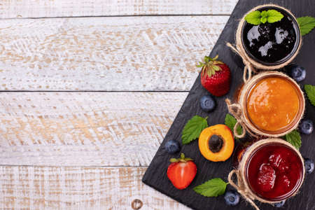 Delicious summer fruits jam - various berries and assorted jams on wooden table - top view, copy...