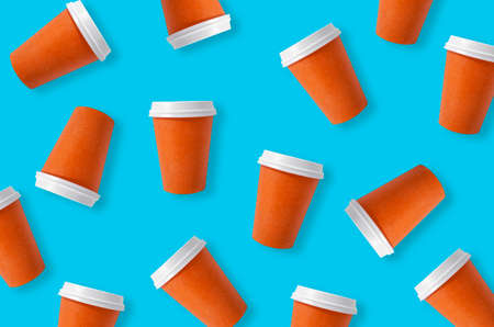 Coffee cup to go. Many plastic orange cups on a blue color background. Disposable cups in a chaotic...