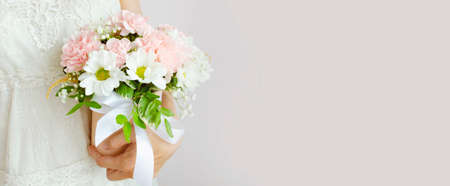 Young woman holding bouquet of flowers in a white dress on a light gray background. Woman with a...
