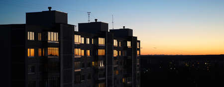 The sunset against the blue sky is reflected in the windows of a multi-storey residential building horizontal bannerの写真素材