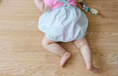 Baby girl crawling on the beige wooden floor at home with pink tee shirt, blue pants and wooden toy