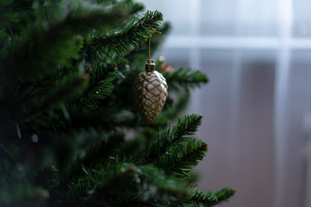 Close-up of a golden pine cone Christmas ornament on an artificial evergreen tree. Elegant...