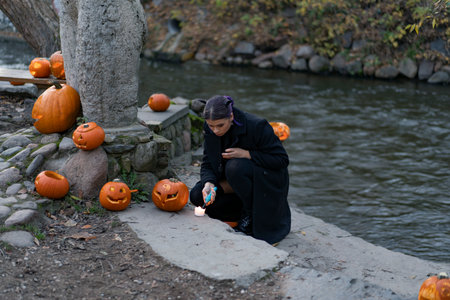 A woman sits on the ground and lights candles in spooky carved faces pumpkins on Halloween eveの写真素材