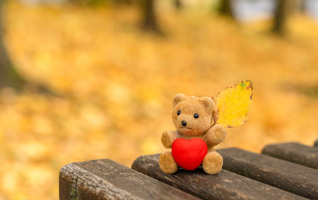 Cute bear toy holding a red heart and autumn leaf, symbolizing love, warmth and coziness of the fall...