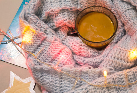 A cup of coffee with milk on a table with knitten blue plaid and garland.