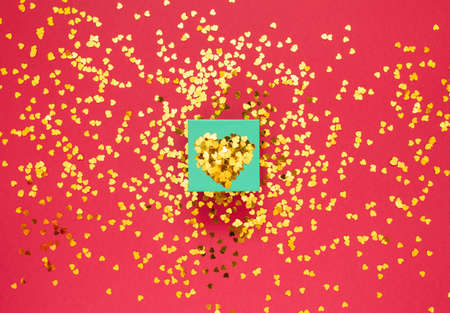 Gift box covered with gold sparkles in the shape of a heart on red background with place for text....
