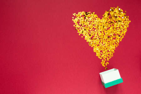 Gold sparkles in the shape of a heart with gift box on red background. Valentines Day, Women's Day. Holiday. Flatlayの写真素材