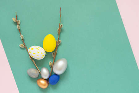 Colored easter eggs with willow branches on color pink and green background. Easter card with empty...