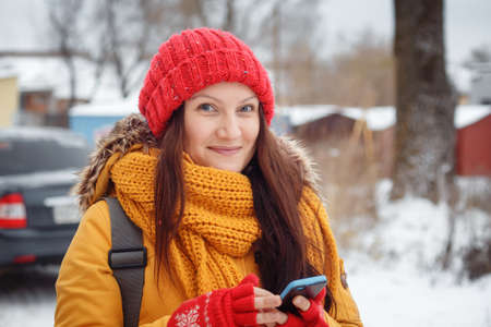 girl in a blue sweater in a bright room standing by the window, holding a phone and looking at the camera!の写真素材