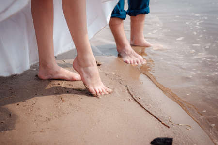 Bride and groom's legs in a wedding dress and in the water. Summer wedding background.の写真素材