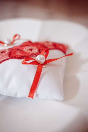 Golden wedding rings on red crimson and white ring pillow with red loveの写真素材