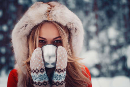beautiful girl is drinking a hot drink from a cup in the winter in nature, tea, coffeeの写真素材