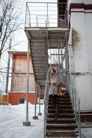 walk around the city: the girl in a gray short fur coat costs on a ladder and looks in a distanceの写真素材