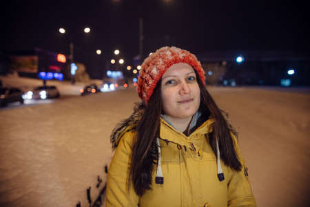 the girl's portrait on a city footpath, in the winter during snowfall, against the background of church, a magnificent fir-tree and a number of lamps. the evening lit with blue firesの写真素材