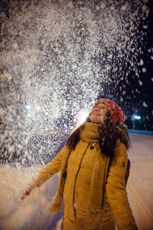 the girl's portrait in the winter who throws up snow. contrast in the light of city lamps. emotions