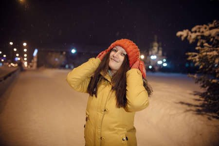 the girl's portrait on a city footpath, in the winter during snowfall, against the background of church, a magnificent fir-tree and a number of lamps. the evening lit with blue firesの写真素材