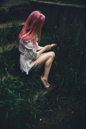 The beautiful girl with pink hair sits on the thrown ladder in an environment of a green grassの写真素材