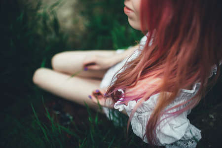 The beautiful girl with pink hair sits on the thrown ladder in an environment of a green grassの写真素材