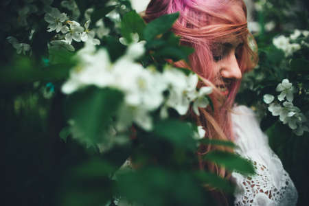 The beautiful girl with pink hair walks among the blossoming apple-tree in the summerの写真素材