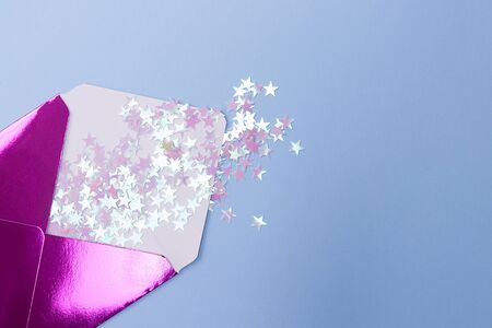 Shiny pink envelope with glitter confetti in a form stars on a blue background. Festive concept.