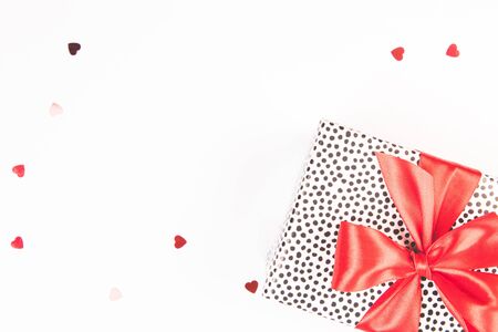 Gift box with red satin bow on a white background with glitter confetti. Festive concept. Isolated.