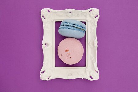 Two colorful macaroons in a white frame on the violet background. Sweety concept.
