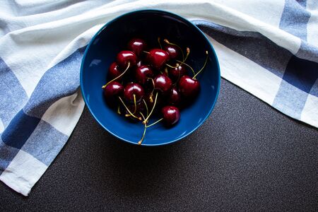 Cherries in a ceramic bowl on a dark background and kitchen towel with a line. Top view. Beautiful...