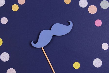 Blue fake mustache with colorful confetti on a dark blue background. Flat lay.の写真素材