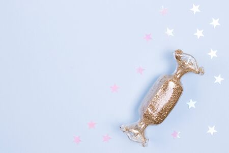 Toy in the shape of holidays candy with the gold glitter and glitter stars on a pastel blue background.の写真素材