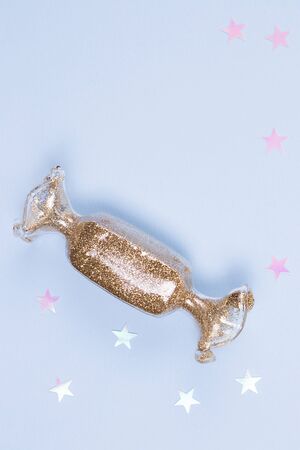 Toy in the shape of holidays candy with the gold glitter and glitter stars on a blue background.の写真素材