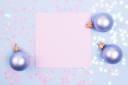 Frame of glitter stars with pink blank card mockup, christmas balls on blue background. Flat lay.の写真素材