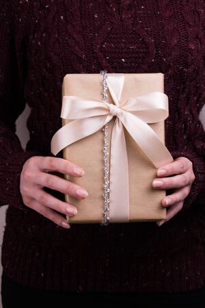 A woman in a purple sweater holds gift box with the beige bow.の写真素材