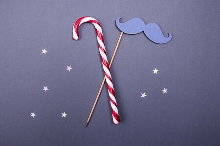 Candy cane and fake mustache witn silver stars confetti on a blue background.の写真素材