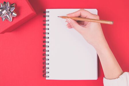 A girl is writing in a notebook with clean pages. Christmas gift box with silver bow. Planning concept.の写真素材