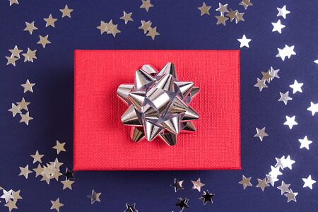 Red gift with a silver shiny bow and sprickle silver stars on a dark blue background. Holiday concept.の写真素材