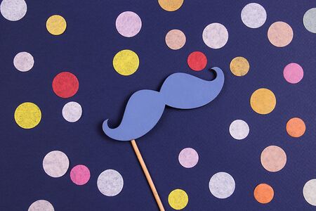Blue fake mustache with a lot of colorful confetti on a dark blue background. Flat lay. Holiday concept.の写真素材