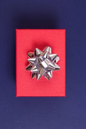 Red gift with a silver shiny bow on a dark blue background. Holiday concept.の写真素材