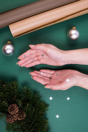 Hands of woman cover stars confetti. Christmas tree wreath, Christmas bowl and design paper on a green background. Holidays concept.の写真素材