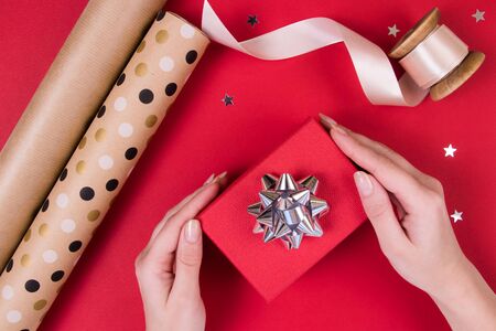 A woman holds a small little box, craft design paper, atlas ribbon on a red background with glitter stars.の写真素材