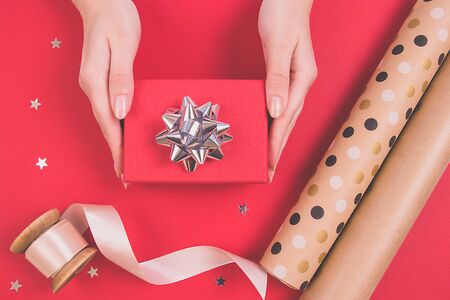 Womans hands holding a red gift with a silver bow on a flat lay background. Sprinkling stars, paper for decor, beige ribbon. Holiday concept.の写真素材