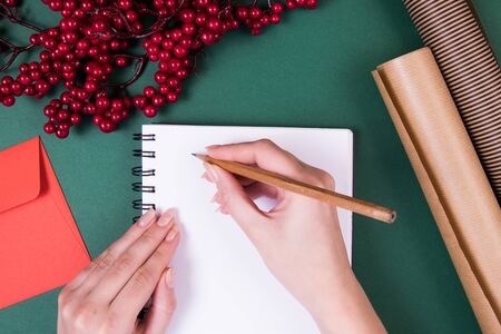 A girl writing in a notebook with clean pages. Christmas decor, design paper, red envelope.の写真素材