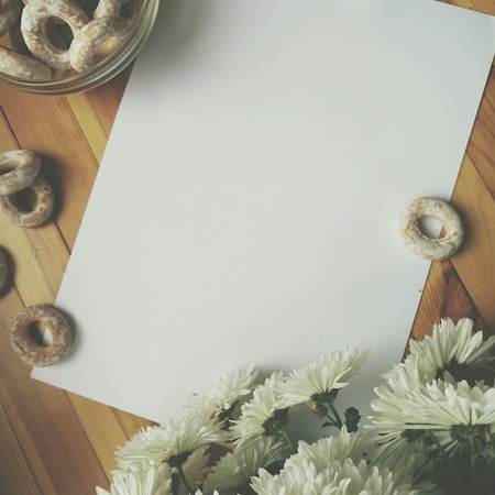 White blank sheet of paper for writing with hands, white flowers and barel lying on wooden table top viewの写真素材