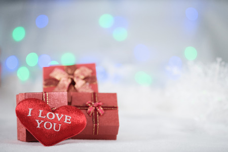 Red gift boxes and heart on the white fur on bokeh background, with copy space for season greeting....