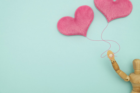Wooden dummy, holding a heart-shaped balloons on blue background with copy space for write and valentine concept.の写真素材
